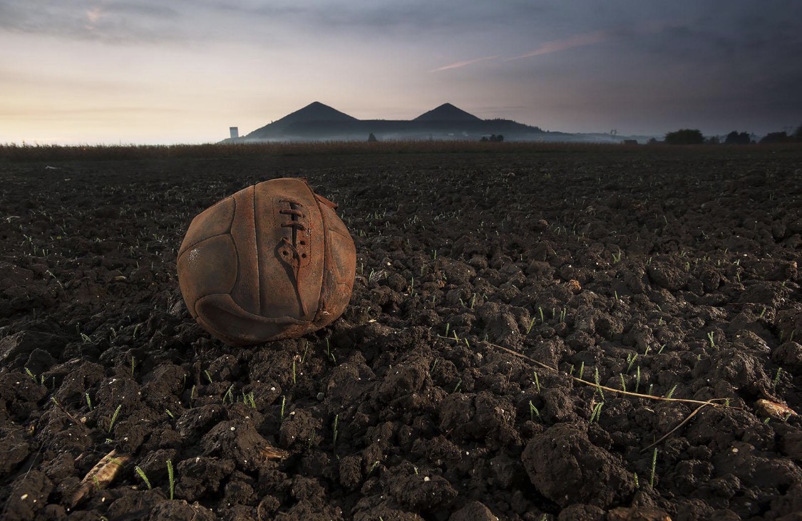 A worn leather ball resting in a field beneath a cloudy sky